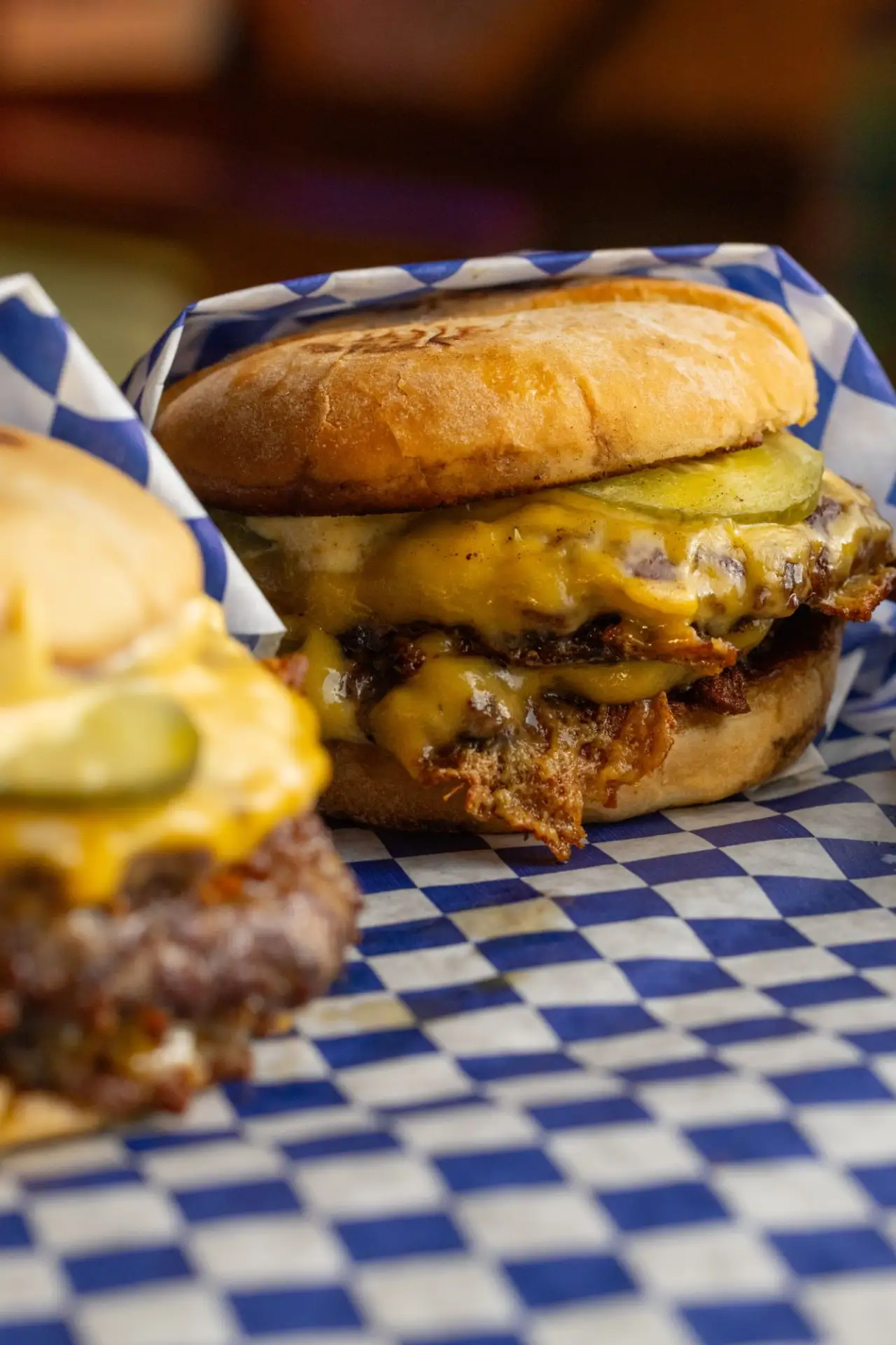 A double cheeseburger with pickles in blue checkered paper