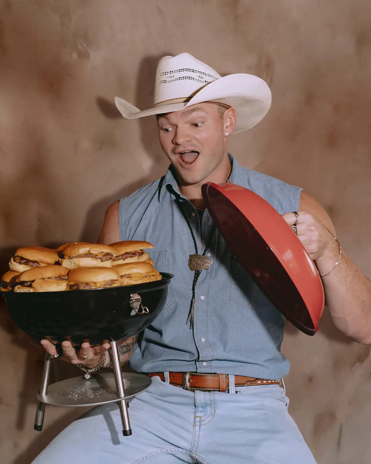 A cowboy lifting the lid on a grill full of smash burgers
